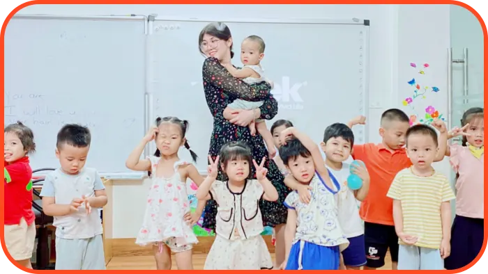 Cô giáo bế em bé cùng các học sinh nhỏ trong lớp